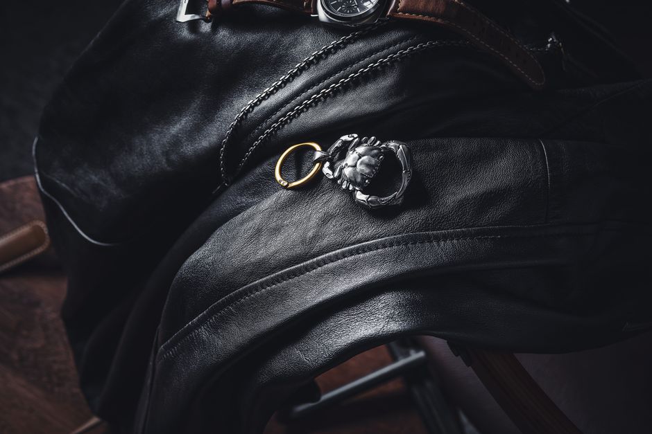 Stylish leather draped with a silver keychain and wristwatch in a moody setting.