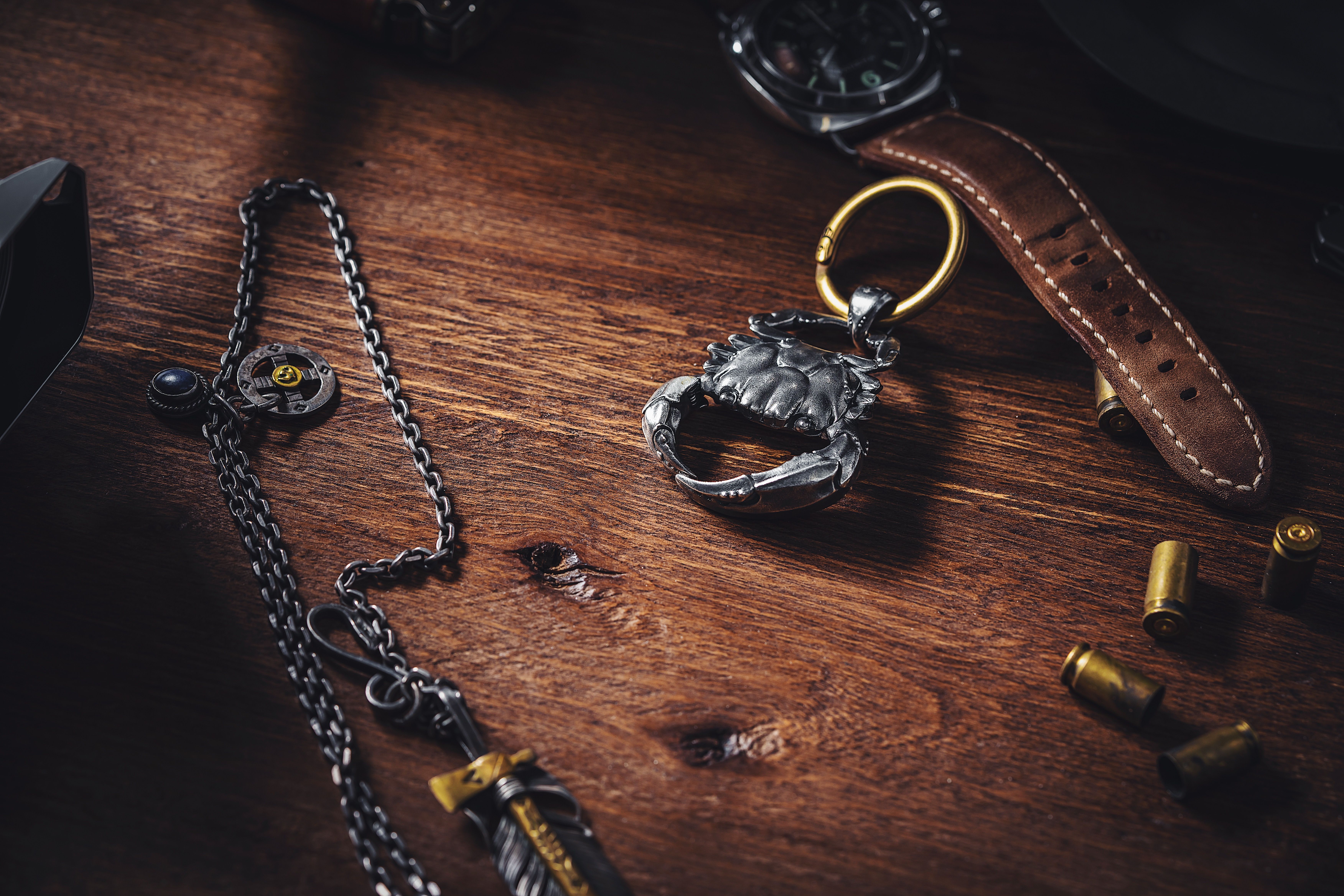 A stylish flat lay featuring a silver crab keychain on a wooden table, surrounded by unique accessories.