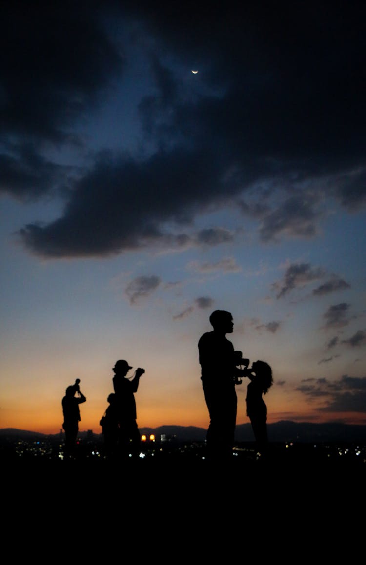 Silhouette Of People Standing And Taking Pictures At Sunset