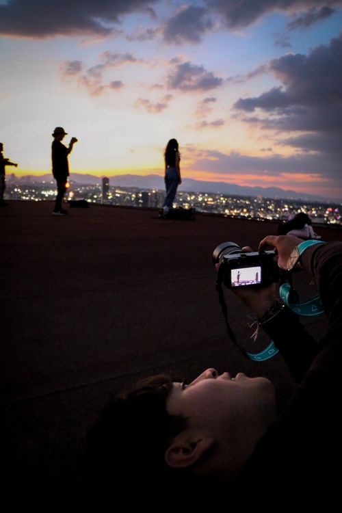 Free Silhouetted photographers capturing a vibrant sunset and city skyline from a rooftop vantage point. Stock Photo