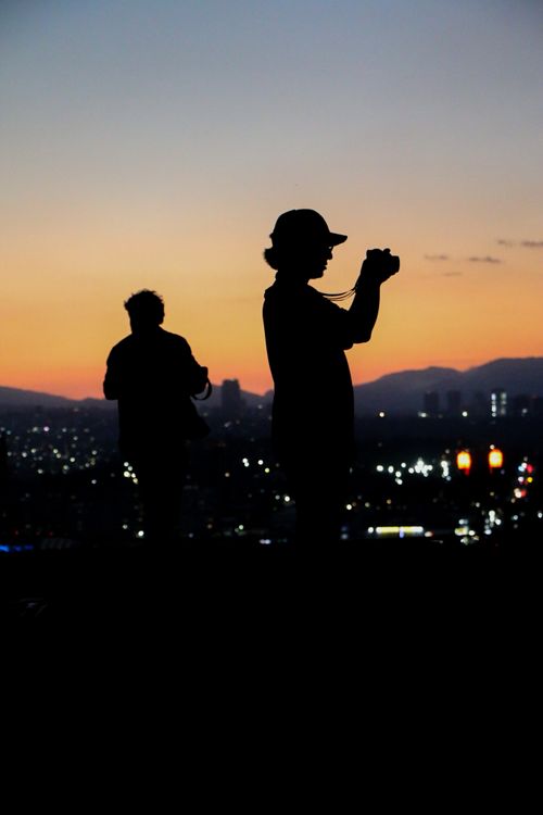 Free Two photographers capture a vibrant cityscape during sunset, highlighted by a colorful sky. Stock Photo