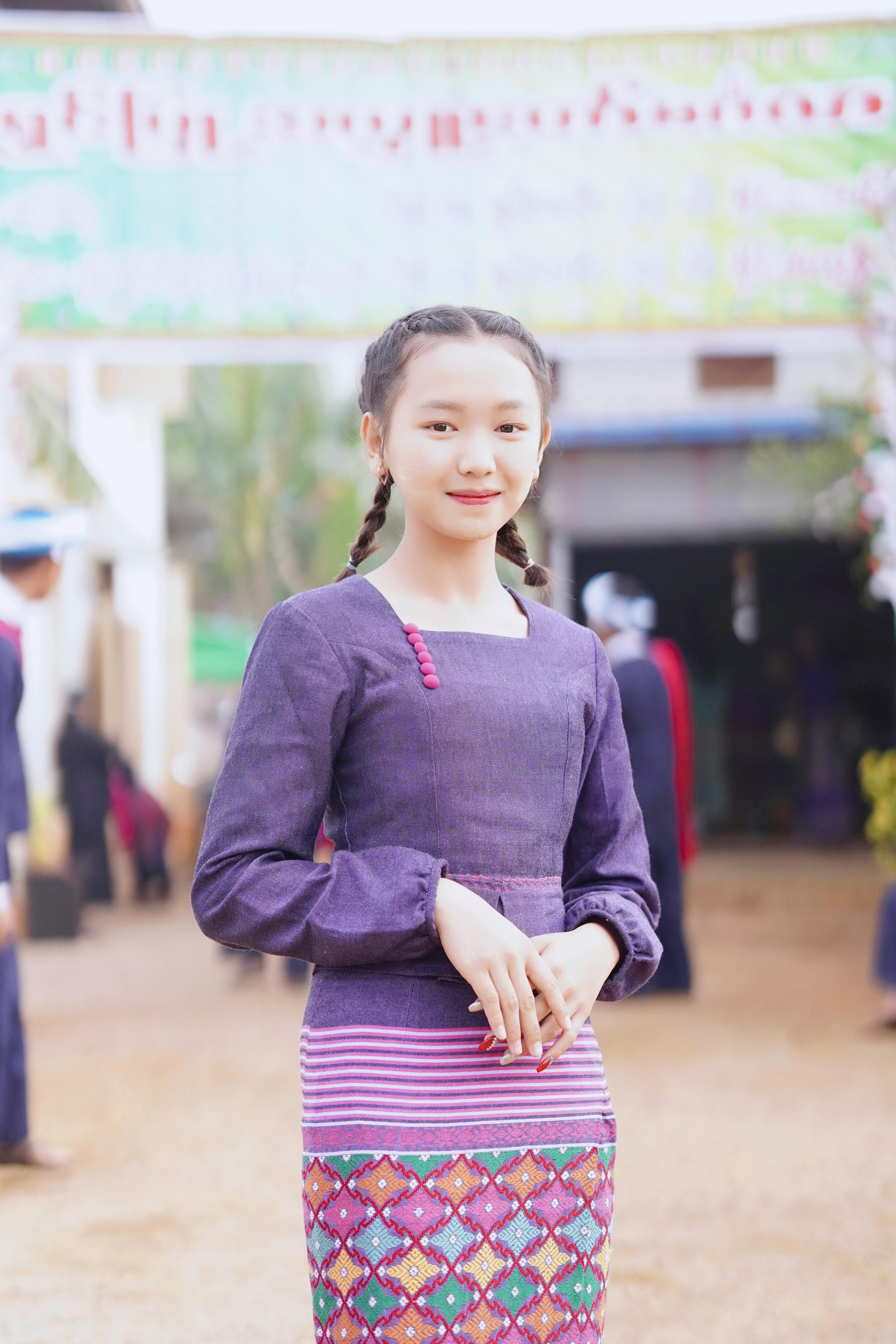 Smiling Asian teenage girl in traditional attire posing outdoors for a vibrant cultural portrait.