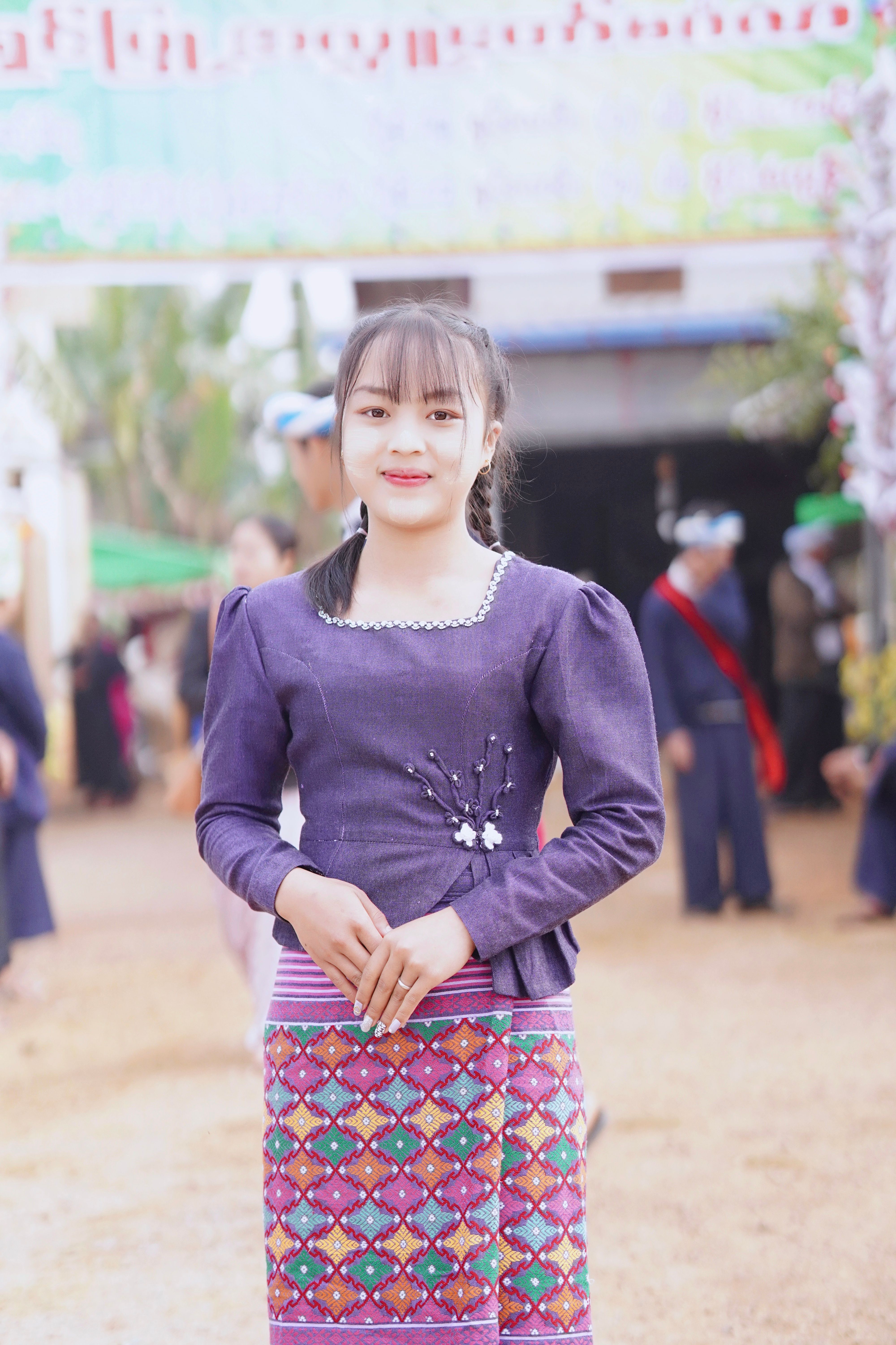 Smiling woman in colorful traditional attire at a vibrant outdoor gathering.