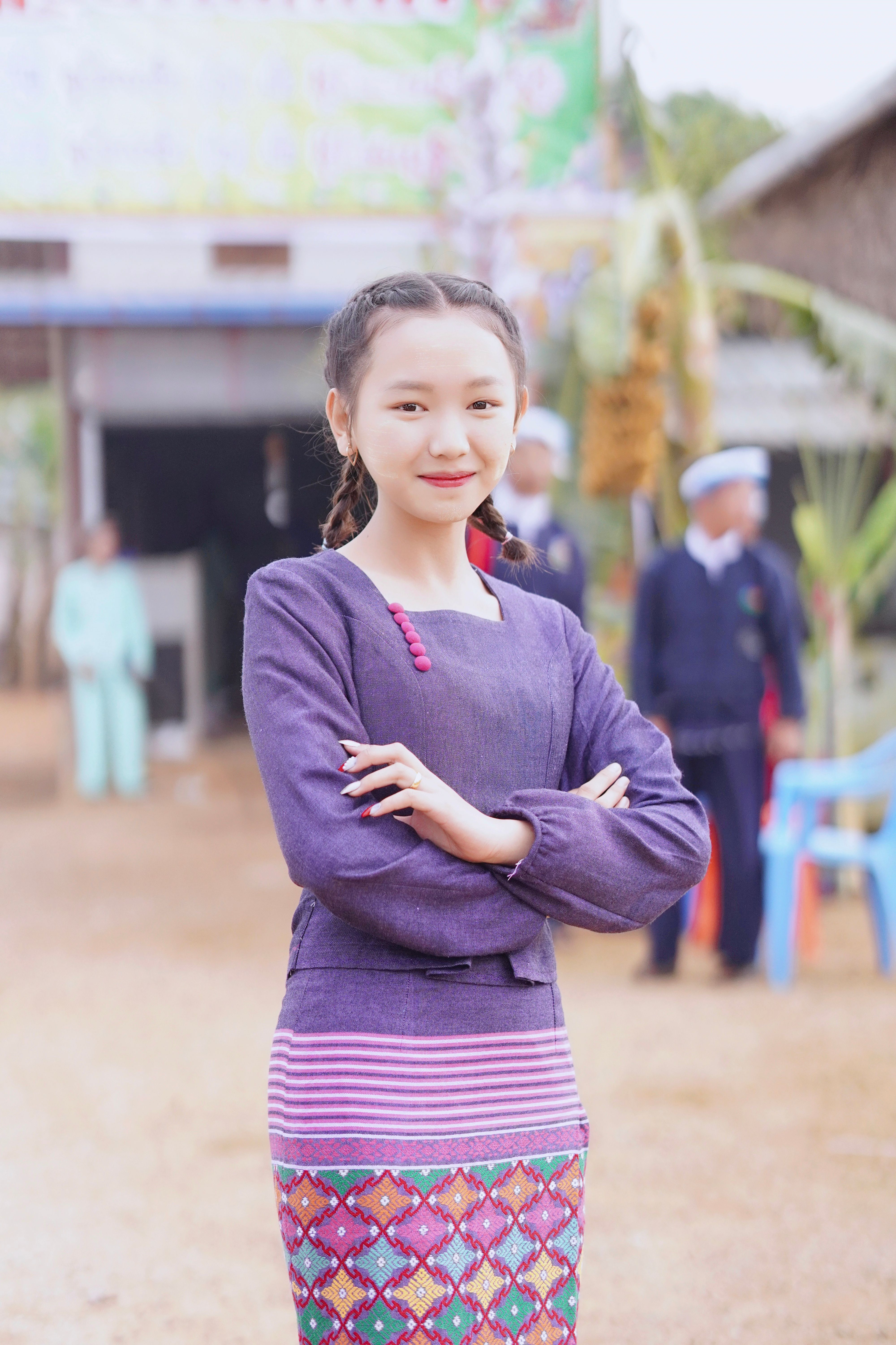Portrait of a smiling young Asian girl in a colorful traditional outfit with braided hair outdoors.