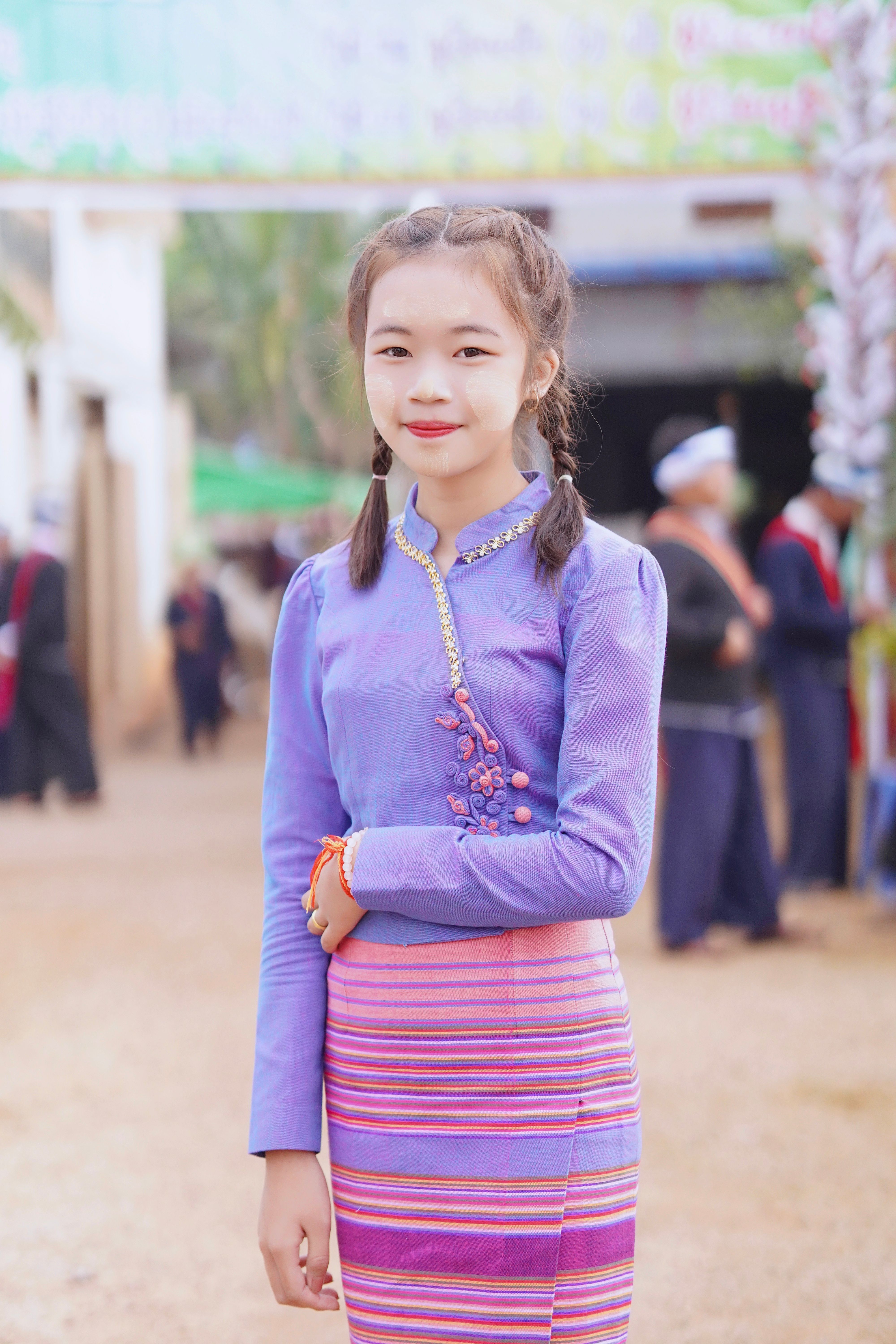 A cheerful young girl poses in traditional colorful clothing outdoors, showcasing vibrant cultural attire.