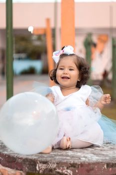 Smiling baby girl in a tutu dress playing with a balloon outside. Bright and joyful moment.