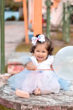Adorable baby girl in a blue tutu with a balloon, smiling outdoors.
