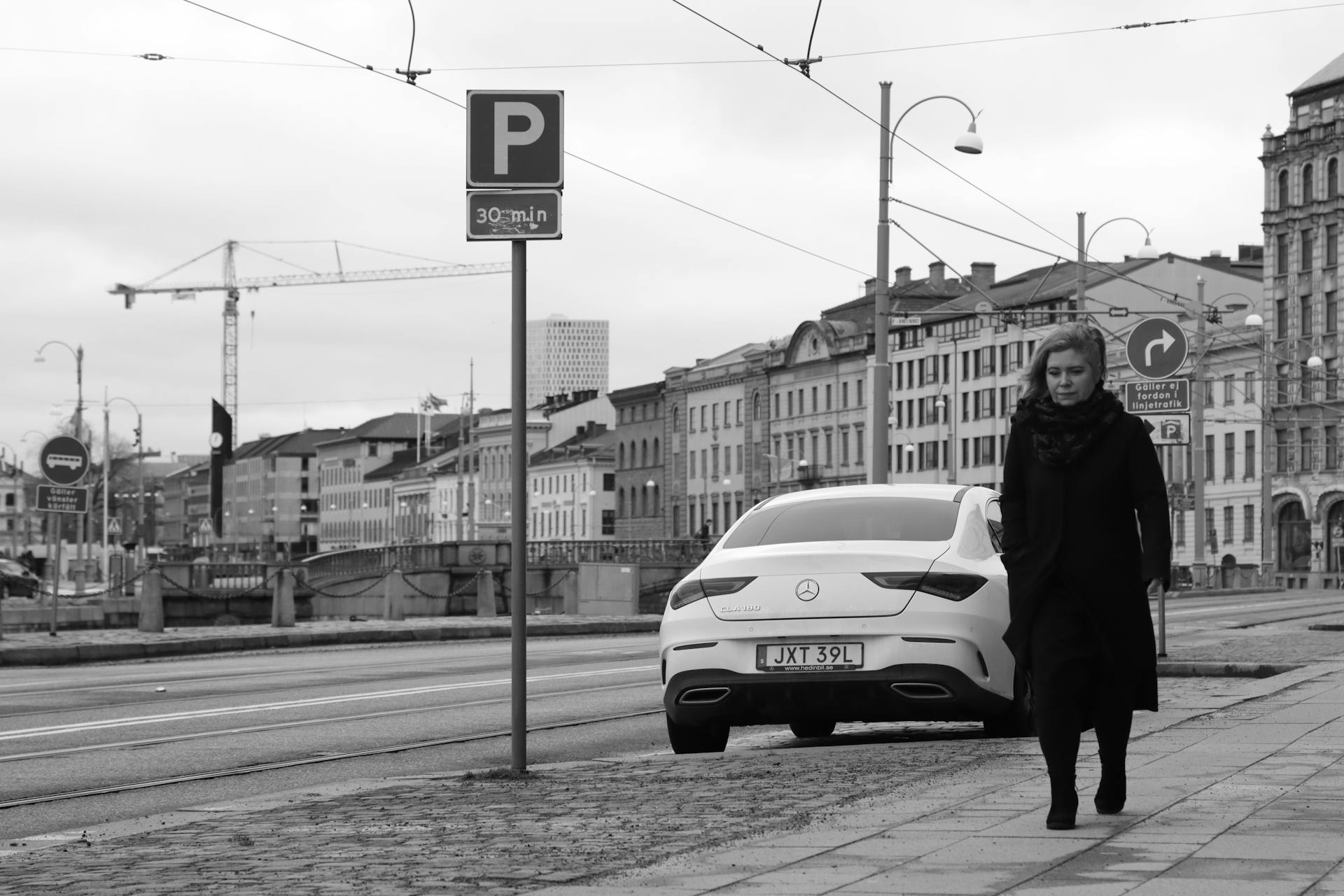 Monochrome view of a city street in Gothenburg featuring a car and a walking woman.