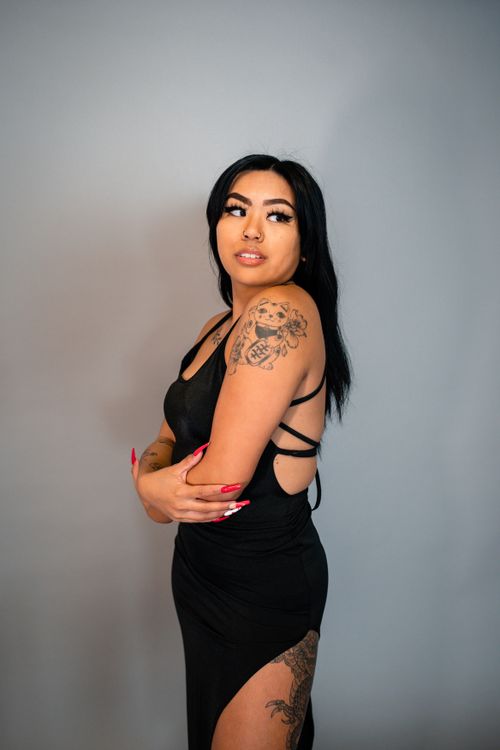 Free Portrait of a stylish woman with tattoos, wearing a black dress against a neutral background. Stock Photo