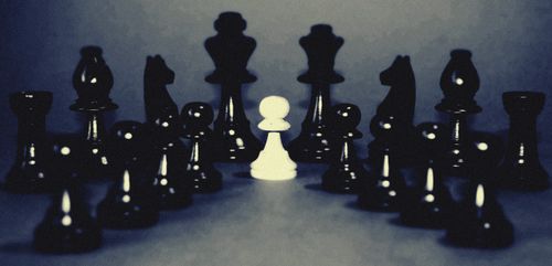 Free A dramatic chessboard with a focus on a single white pawn among black pieces, illustrating strategy. Stock Photo