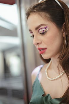 Close-up portrait of a woman with artistic makeup and pearl jewelry indoors.