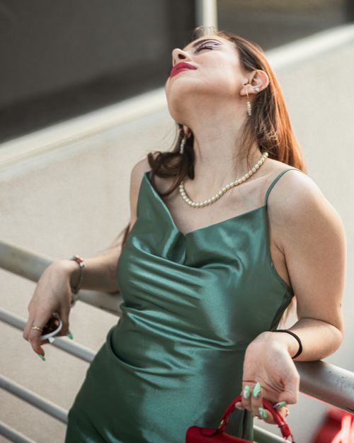Free Chic woman in a glamorous green dress striking a relaxed pose outdoors, exuding elegance. Stock Photo