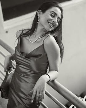 Chic woman in a black dress with white makeup poses indoors, embodying modern elegance.