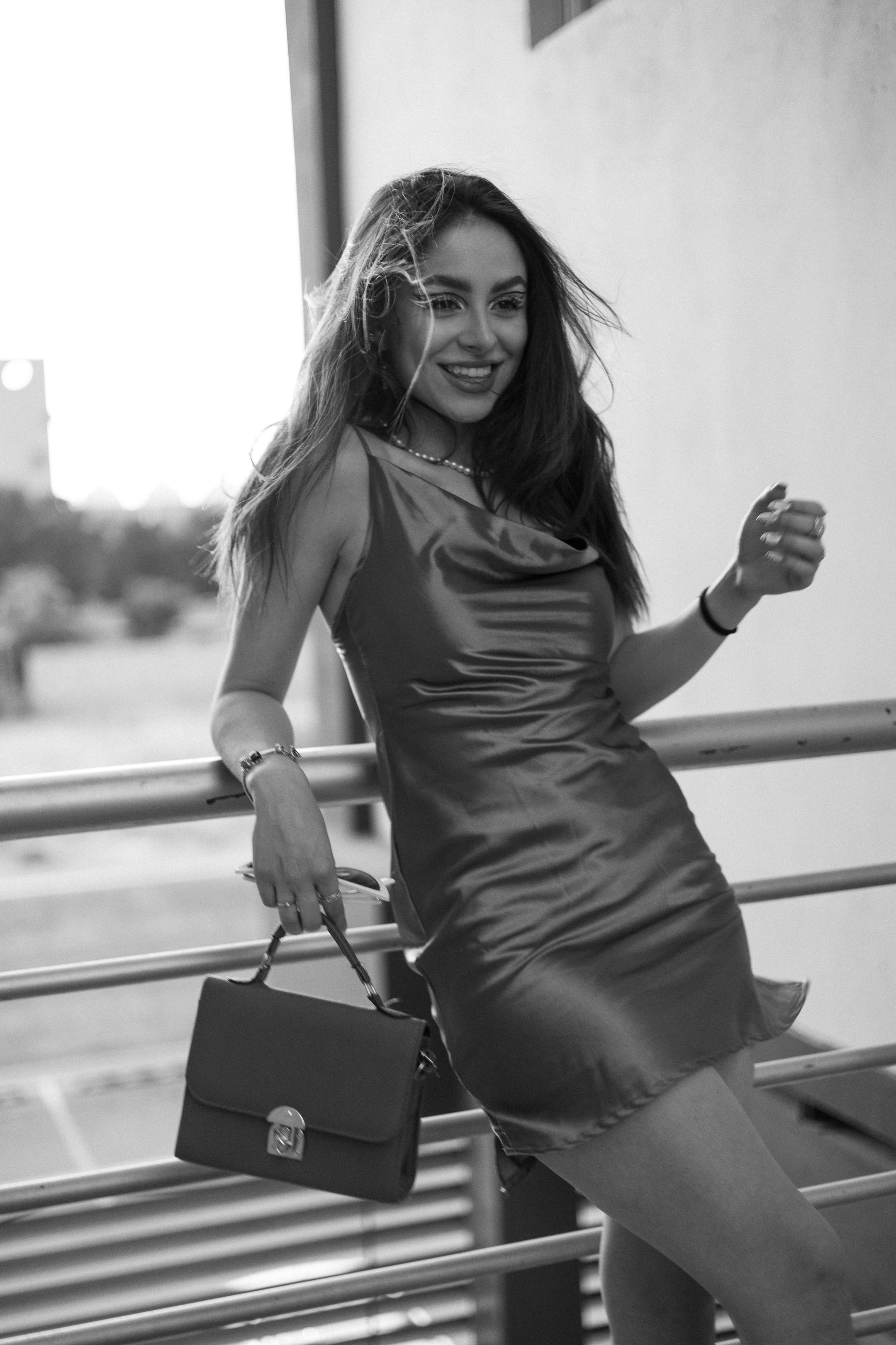 Free Fashionable woman in a sleek dress posing outdoors, carrying a purse. Stock Photo