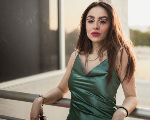 Free Glamorous portrait of a woman in a green satin dress with striking makeup, set in soft lighting. Stock Photo