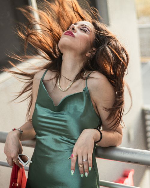 Free A stylish woman in a green dress poses outdoors, her hair blowing in the wind, exuding confidence and grace. Stock Photo