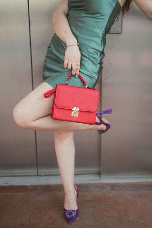 Free Fashionable woman posing with a red handbag and green dress, showcasing modern style and elegance. Stock Photo