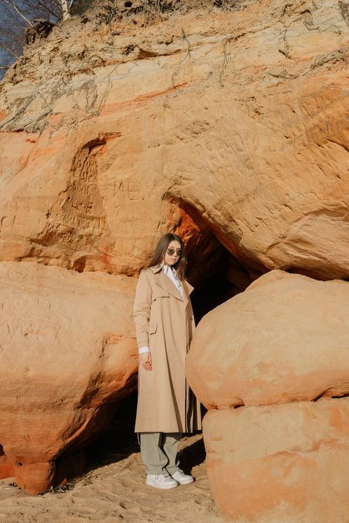 Free A person in a trench coat stands by sandstone rocks, showcasing earthy adventure. Stock Photo