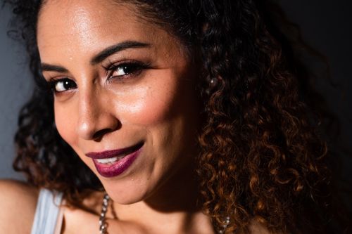 Free Close-up portrait of a smiling woman with curly hair and makeup, exuding elegance and confidence. Stock Photo