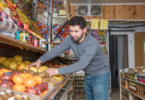 Free Grocery store worker organizing fresh fruits and vegetables on display shelves. Stock Photo