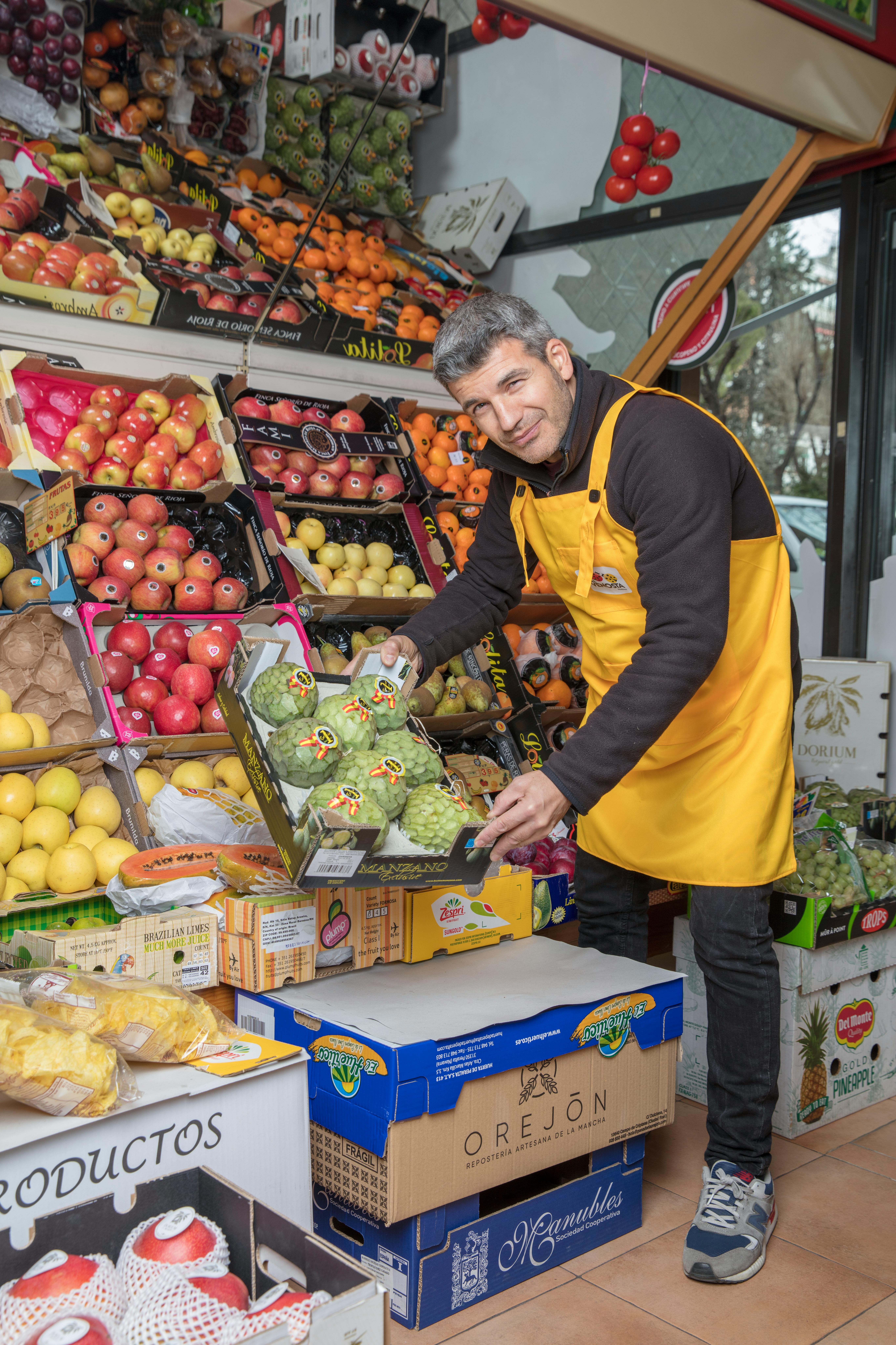 A cheerful grocery clerk organizing fresh produce in a vibrant, colorful market setting.