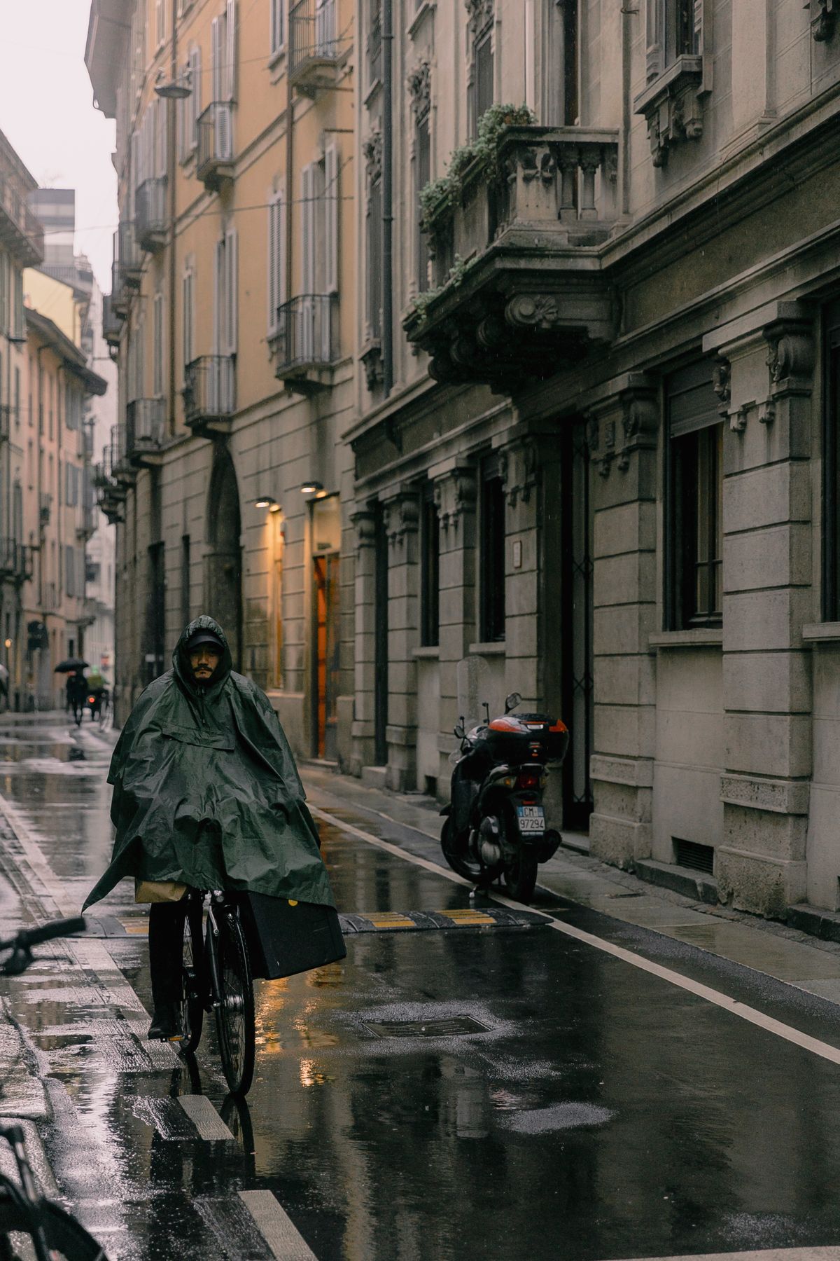 Cyclist wearing a raincoat riding along a wet city street