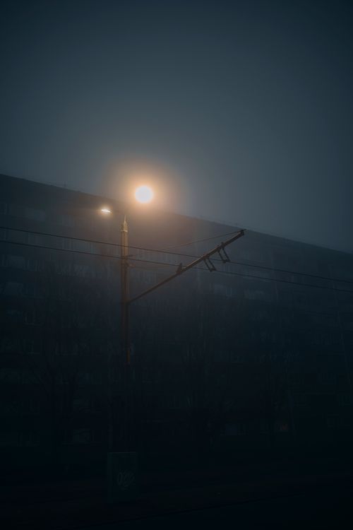 Free Atmospheric fog envelops a dimly lit street scene, featuring a glowing street lamp. Stock Photo