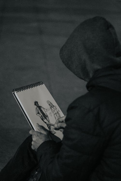 Person in Hood Drawing in Notebook