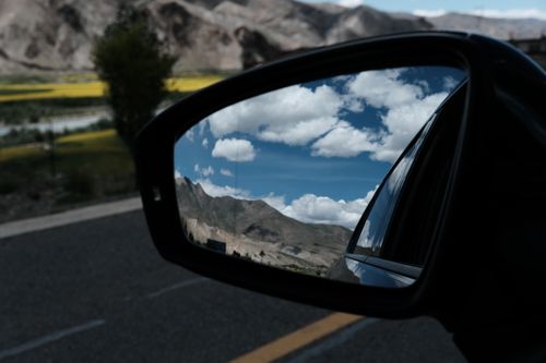 Free A car mirror reflects beautiful mountains and a blue sky with clouds, creating a picturesque travel scene. Stock Photo