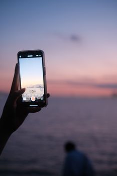 A smartphone capturing a beautiful sunset over the sea, highlighting modern technology use.