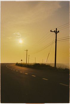 Curved rural road at sunset with power lines and a glowing horizon.