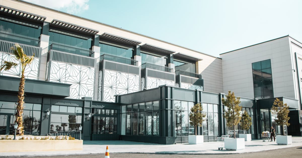 Contemporary glass building with palm trees and modern design in a city setting, sunny day.