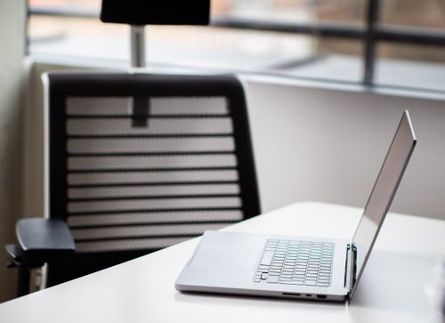 Free A sleek laptop on a white desk in a contemporary office setting with mesh chair. Stock Photo