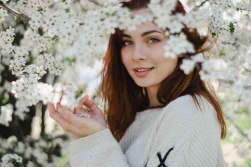 Free Young woman in spring, smiling gently, surrounded by blossom flowers. Stock Photo