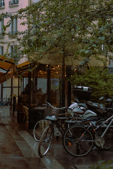 Scenic Paris street view featuring bicycles parked by a quaint café under rainy weather.