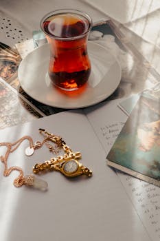 A warm cup of tea with gold jewelry and notes, creating a luxurious and artistic atmosphere.