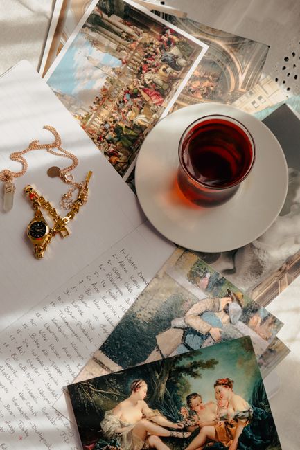 A vintage-themed still life featuring a coffee, jewelry, and historical prints.