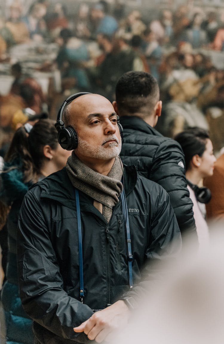 Man With Gray Beard Wearing Headphones And Standing In The Crowd 