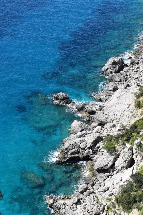Free Sunlit coastline with eroded rocks and clear blue sea viewed from above. Stock Photo