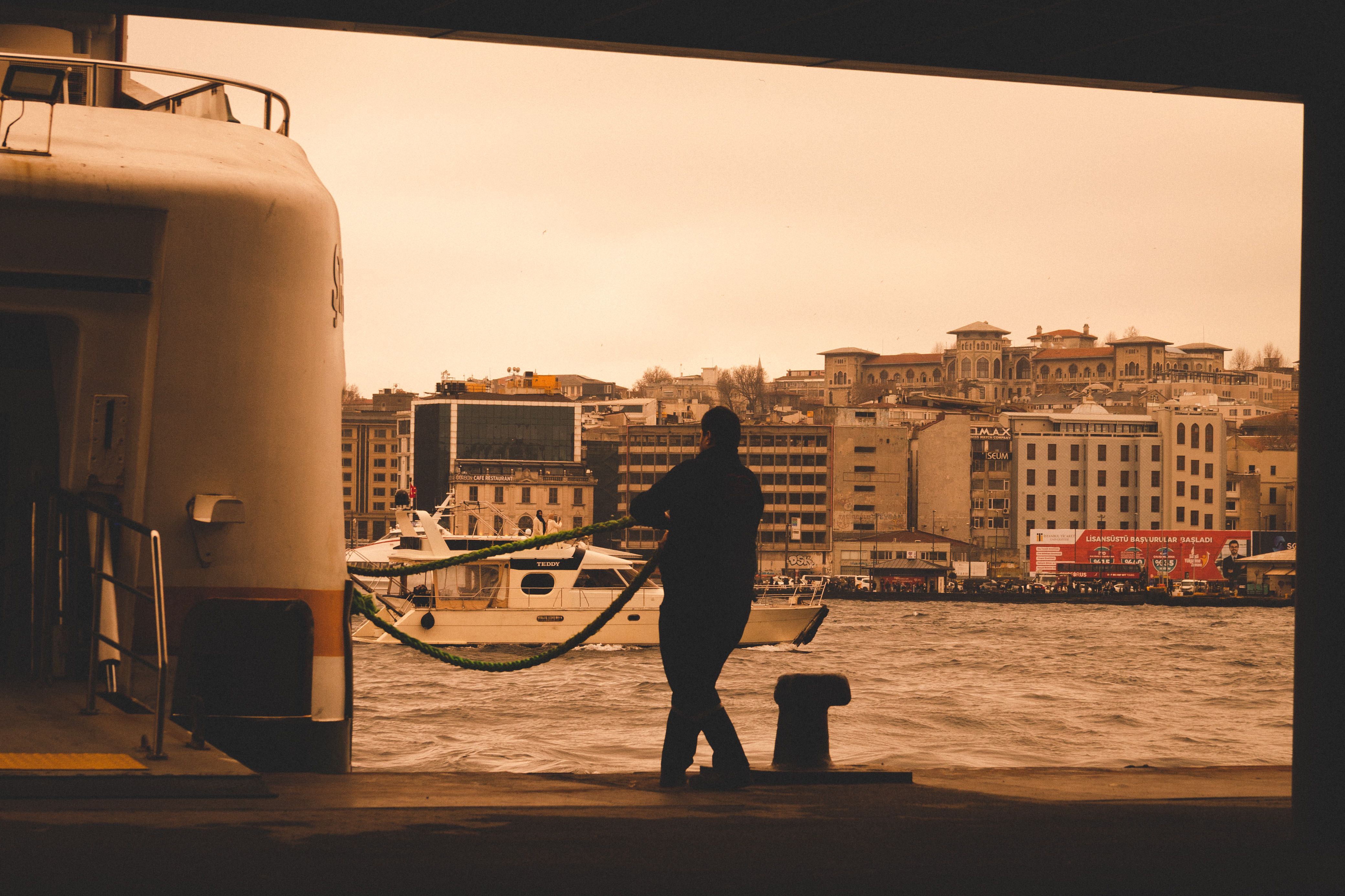 Silhouette of a man on a ferry deck with a cityscape view in sepia tones, capturing a waterfront scene.