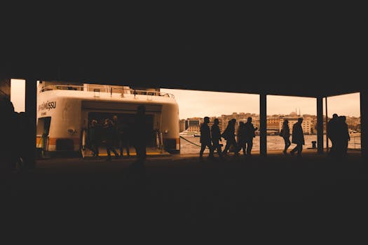 Silhouettes of passengers boarding a ferry with city skyline at sunset captured in warm sepia tones.