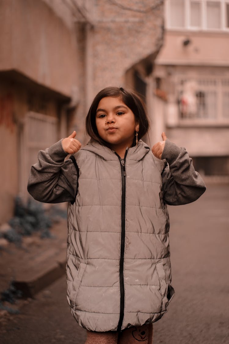 Young Girl In A Jacket Standing On The Street And Showing Thumbs Up 