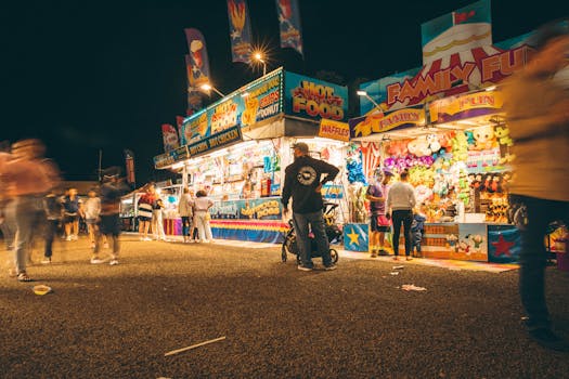 A lively night fair with illuminated stalls, games, and blurred motion of people.