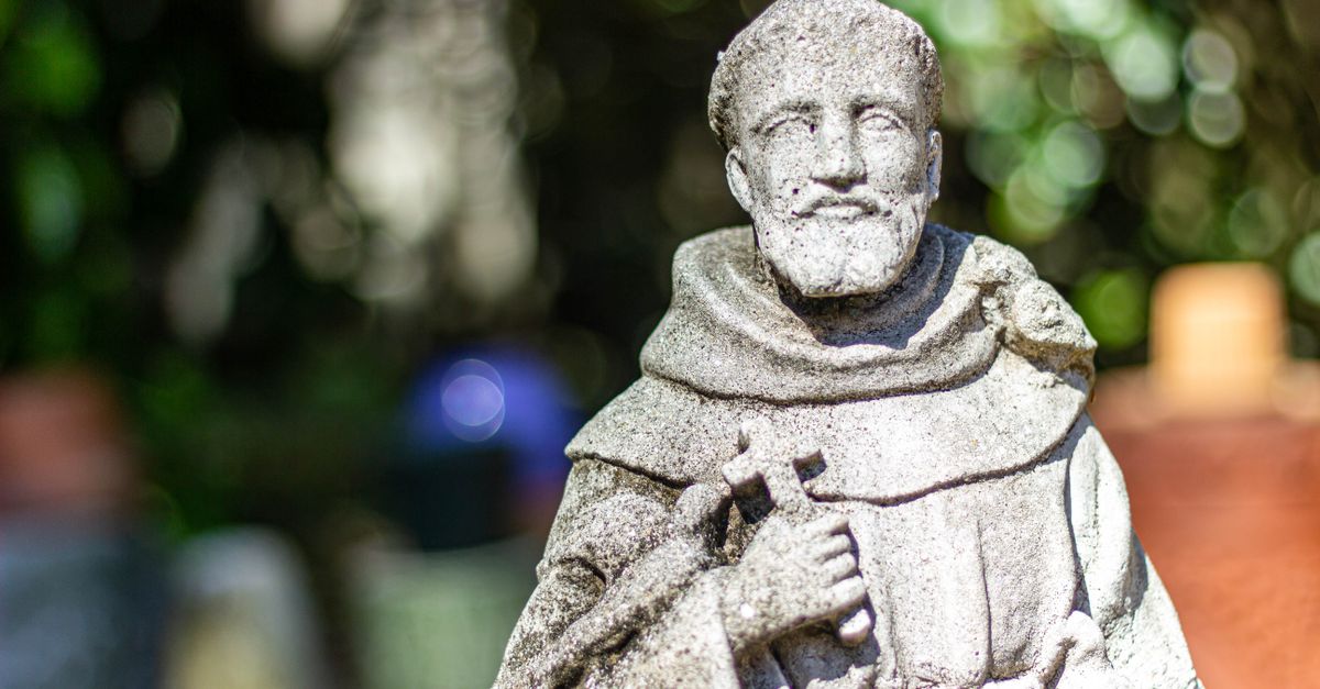 A serene stone statue of Saint Francis holding a cross in Gainesville, Florida.