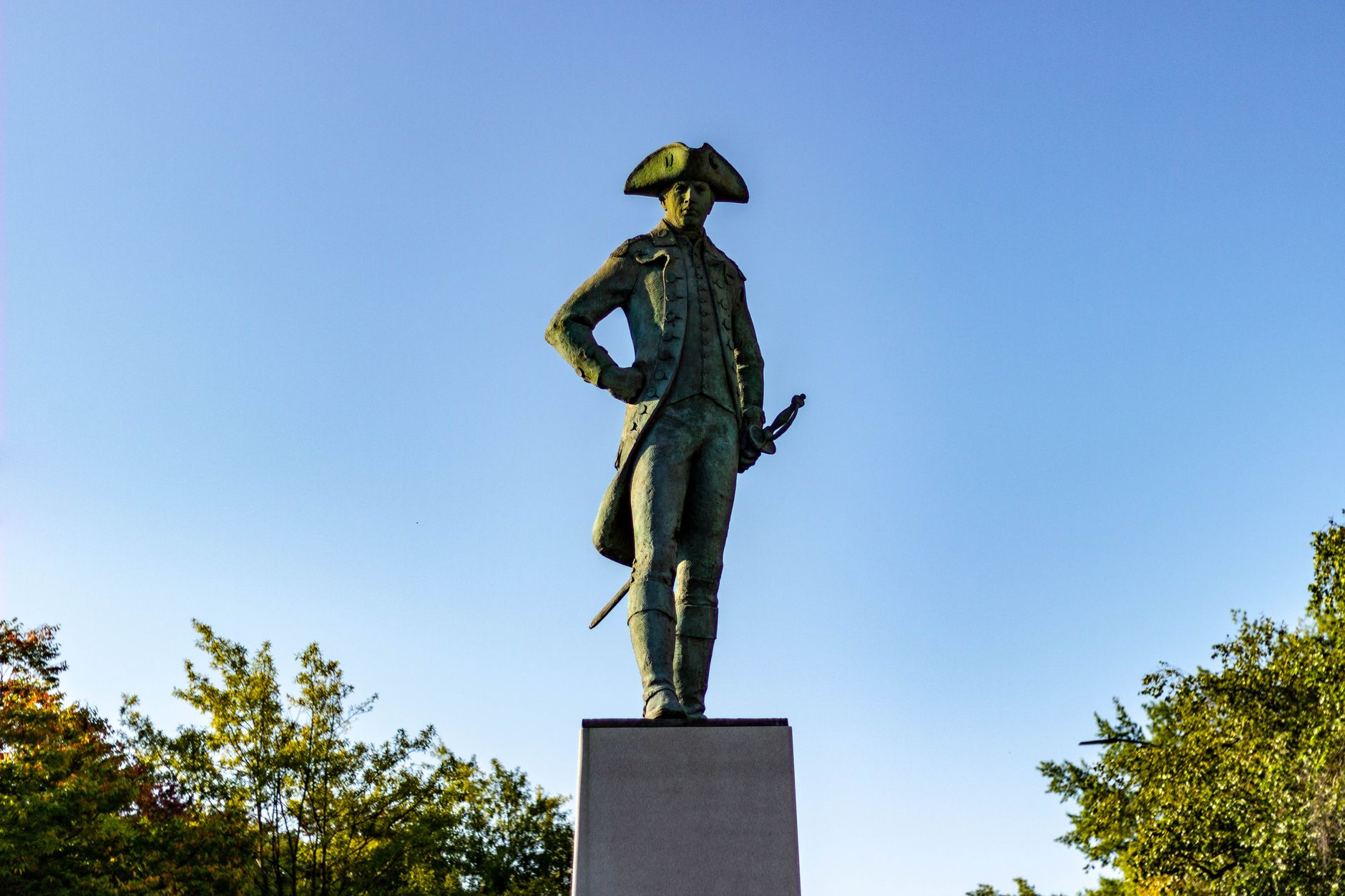 A commanding statue of Nathanael Greene against a clear blue sky in a Rhode Island park.