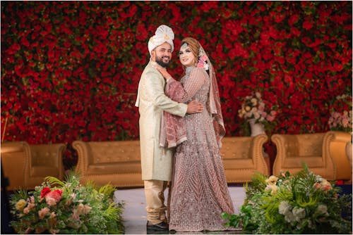 Bride and Groom in Traditional Clothing Posing on the Background of a Flower Arrangement 