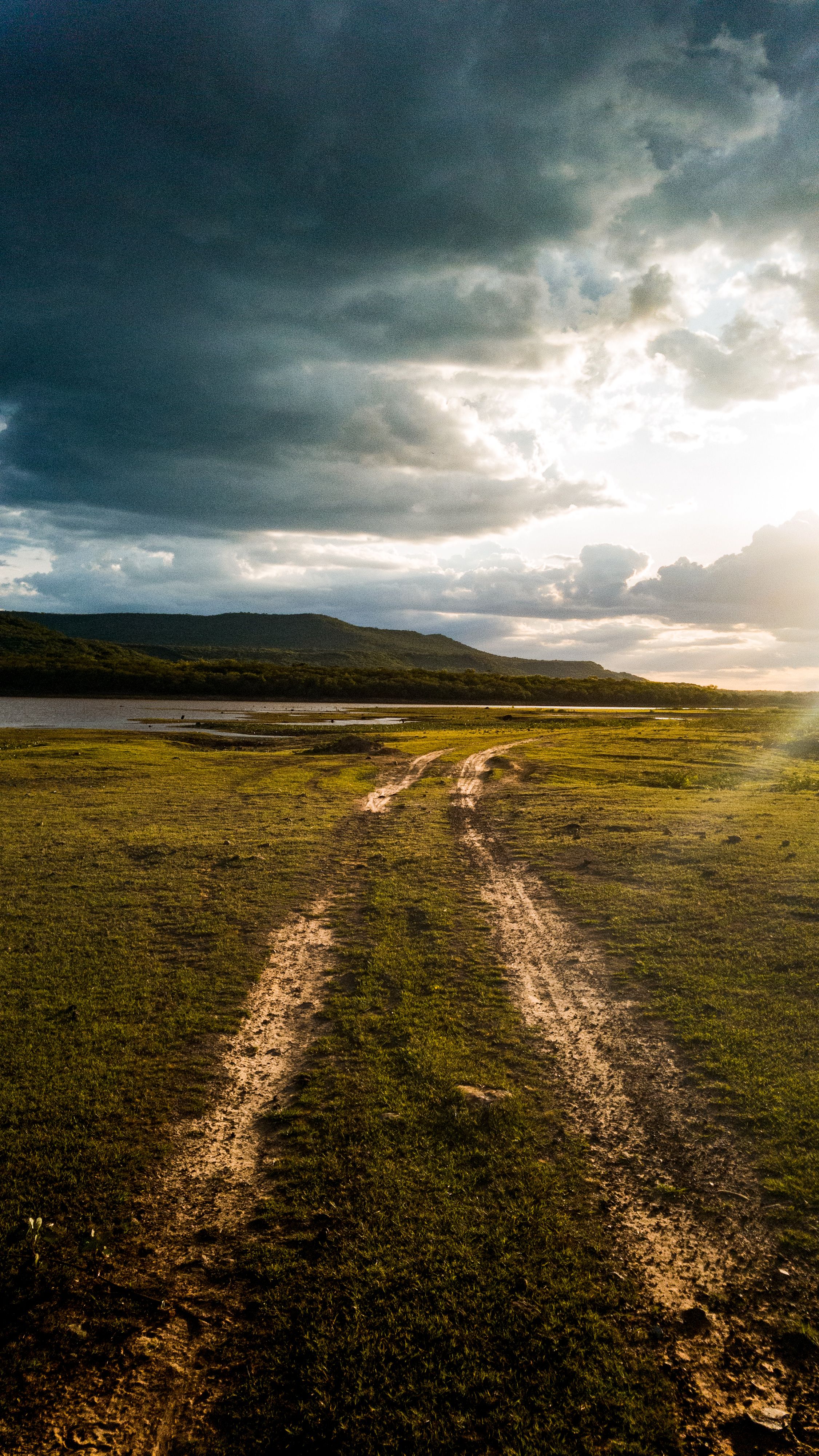 A dirt road leading to a grassy field with a sun setting behind it ...