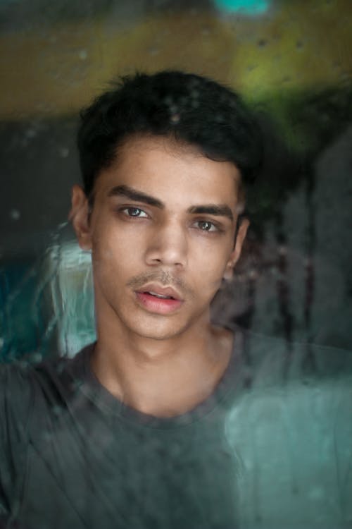 Young Man with Dark Hair Photographed from behind a Wet Window 