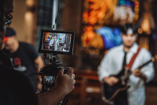 Close-up shot of hands holding a camera recording a guitarist during a live performance.