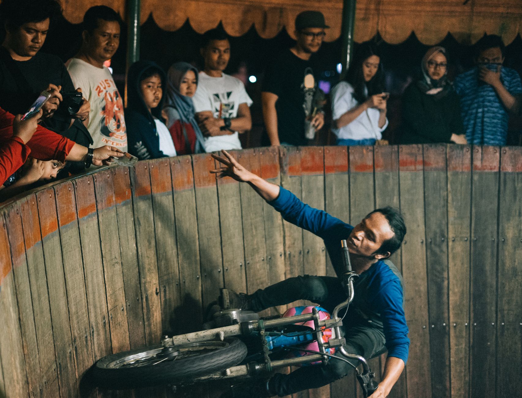 A biker performs a thrilling stunt on a wall of death surrounded by an eager audience.